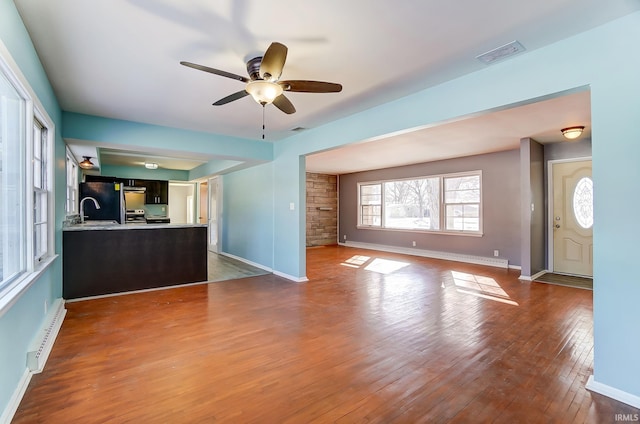 unfurnished living room featuring ceiling fan, wood-type flooring, sink, and a baseboard radiator