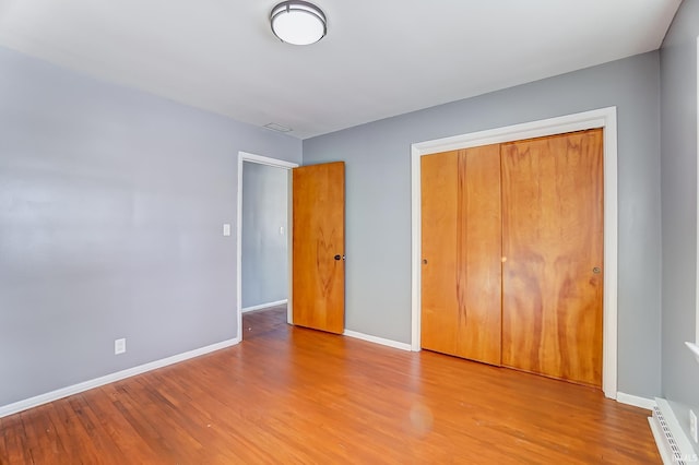 unfurnished bedroom featuring hardwood / wood-style flooring, a baseboard heating unit, and a closet