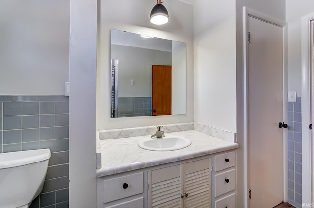 bathroom featuring toilet, tile walls, and vanity