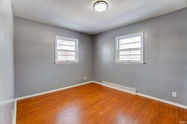 empty room featuring baseboard heating, a healthy amount of sunlight, and hardwood / wood-style floors