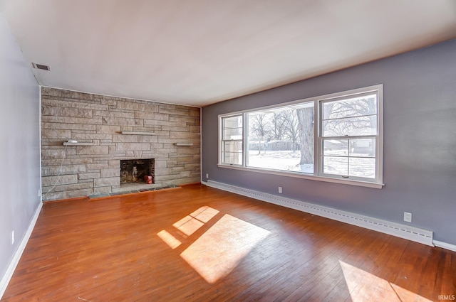 unfurnished living room featuring baseboard heating, a wealth of natural light, light wood-type flooring, and a fireplace