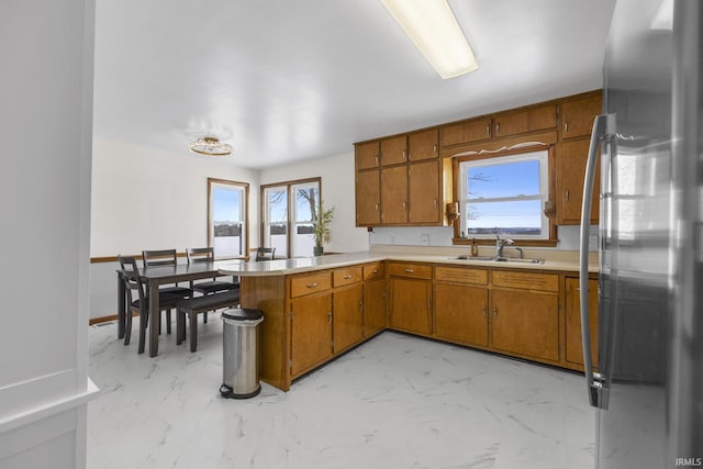 kitchen with stainless steel refrigerator, kitchen peninsula, a healthy amount of sunlight, and sink