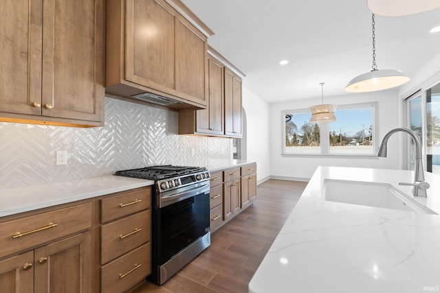 kitchen featuring light stone countertops, stainless steel gas range, hanging light fixtures, backsplash, and sink