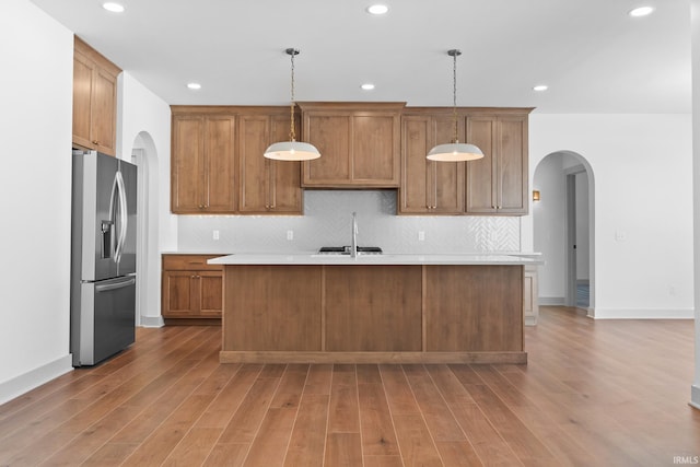 kitchen with sink, hardwood / wood-style floors, stainless steel fridge with ice dispenser, a center island with sink, and pendant lighting