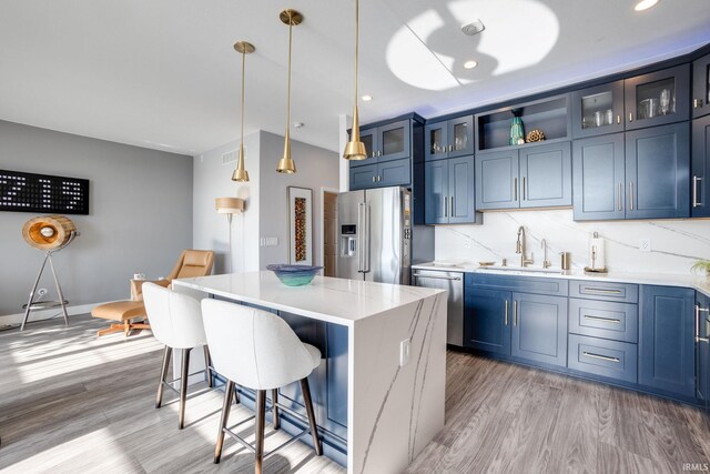 kitchen with pendant lighting, a center island, backsplash, blue cabinetry, and appliances with stainless steel finishes