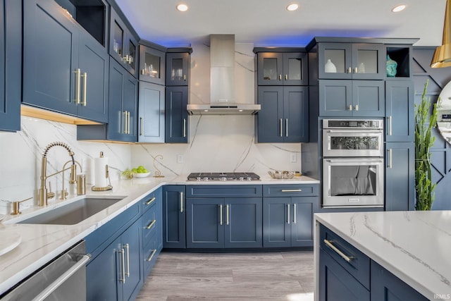 kitchen featuring stainless steel appliances, light stone countertops, wall chimney exhaust hood, and sink