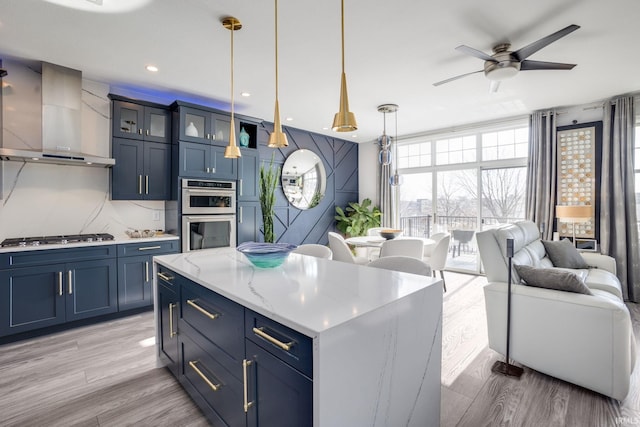 kitchen with floor to ceiling windows, light wood-type flooring, appliances with stainless steel finishes, and wall chimney exhaust hood