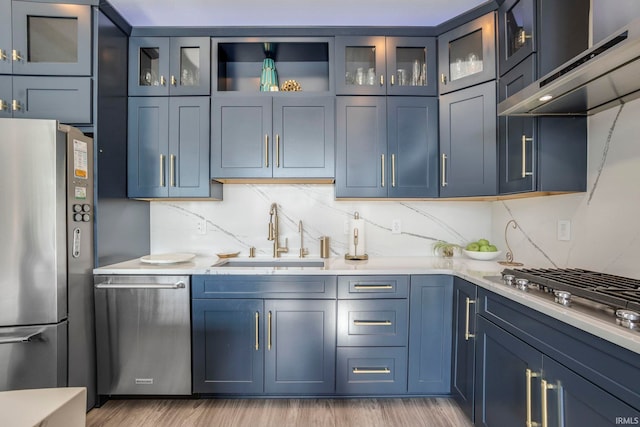 kitchen with appliances with stainless steel finishes, blue cabinetry, sink, and wall chimney exhaust hood