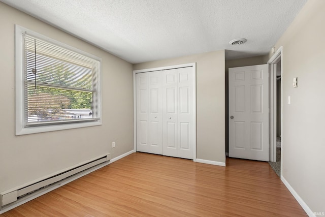 unfurnished bedroom featuring a textured ceiling, light hardwood / wood-style flooring, a closet, and a baseboard heating unit