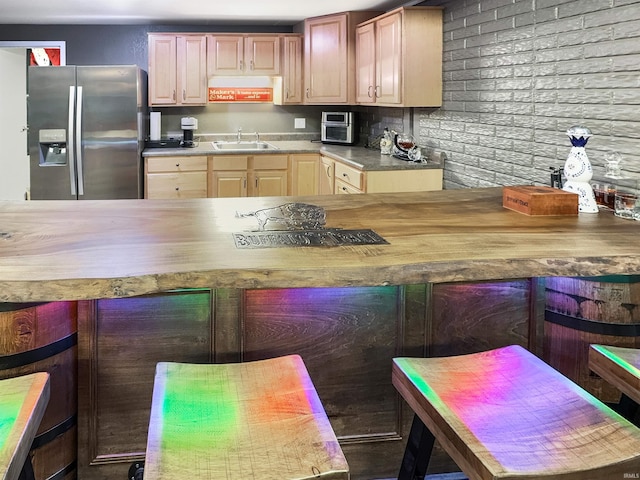 kitchen featuring stainless steel fridge, a kitchen bar, a sink, and light brown cabinetry