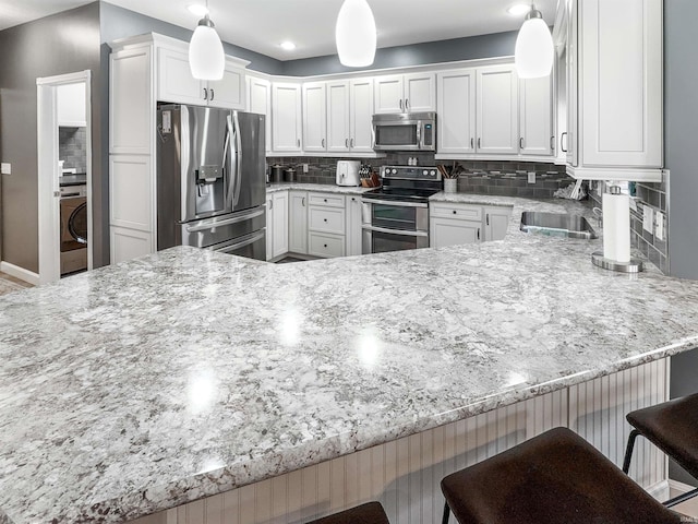 kitchen with a sink, white cabinetry, appliances with stainless steel finishes, decorative backsplash, and light stone countertops