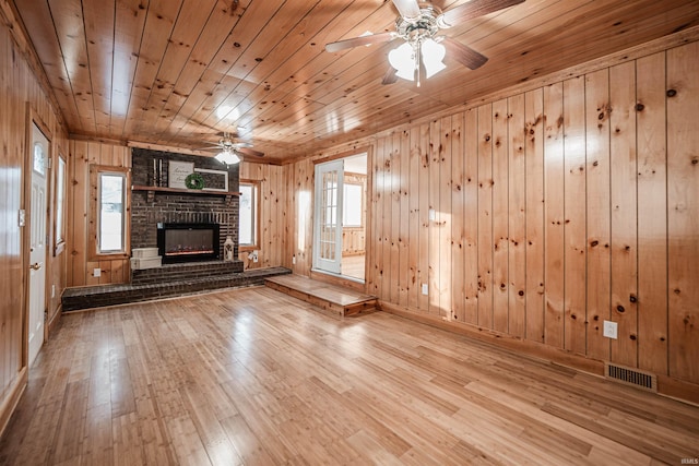 unfurnished living room with wooden walls, wooden ceiling, a brick fireplace, and light hardwood / wood-style floors