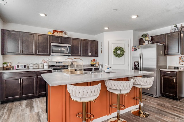 kitchen featuring a textured ceiling, stainless steel appliances, a center island with sink, light hardwood / wood-style floors, and a kitchen bar