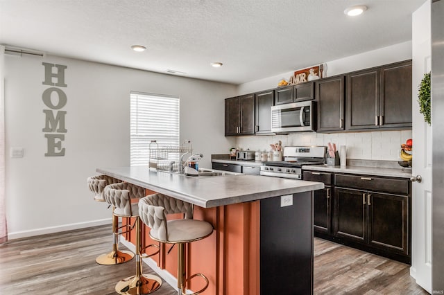 kitchen featuring stainless steel appliances, a center island with sink, decorative backsplash, a breakfast bar area, and sink