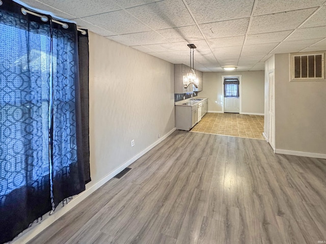 basement with light wood-type flooring, a chandelier, a paneled ceiling, and sink