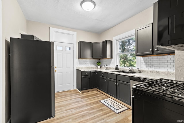 kitchen featuring sink, light hardwood / wood-style floors, tasteful backsplash, stainless steel refrigerator, and gas range