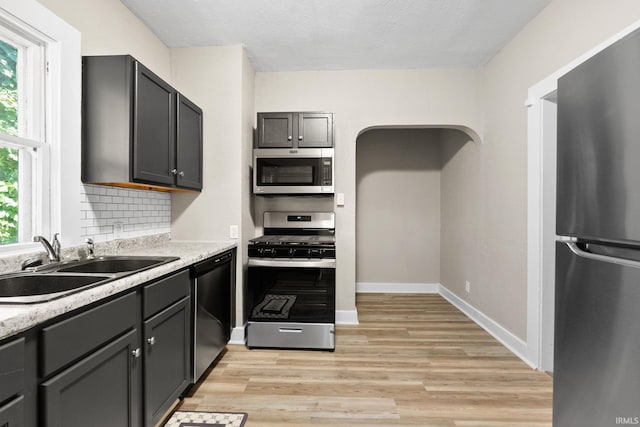 kitchen featuring gray cabinets, stainless steel appliances, light wood-type flooring, sink, and tasteful backsplash