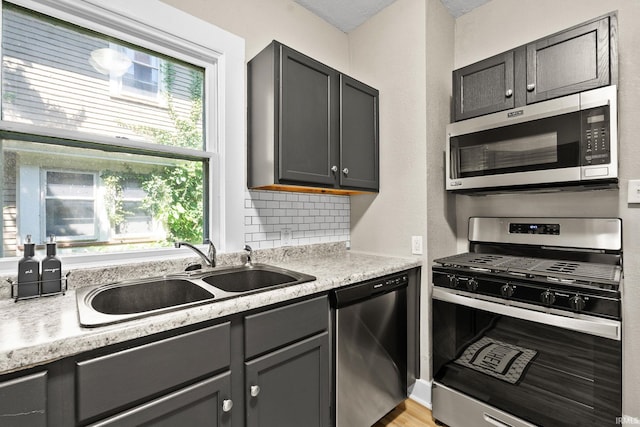 kitchen with sink, backsplash, light stone countertops, gray cabinetry, and appliances with stainless steel finishes