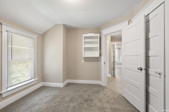 spare room with lofted ceiling, a textured ceiling, and light colored carpet