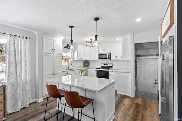 kitchen with hanging light fixtures, stainless steel appliances, a kitchen island, backsplash, and white cabinets