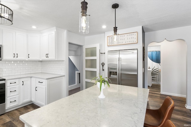 kitchen with light stone counters, stainless steel appliances, white cabinets, and pendant lighting