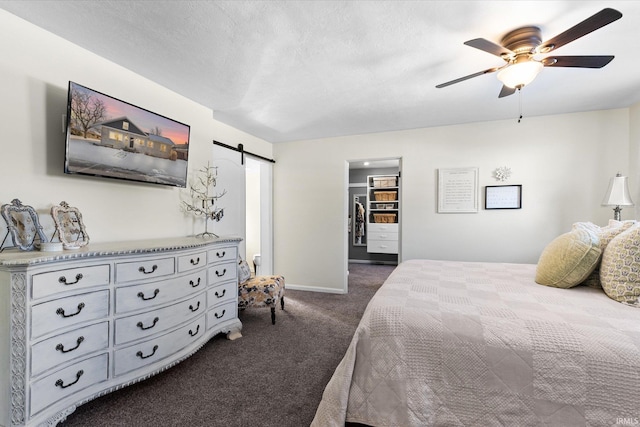 bedroom with a closet, a barn door, a walk in closet, ceiling fan, and dark carpet