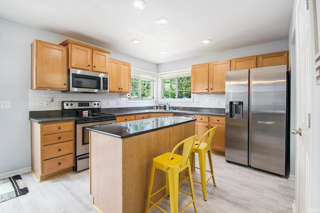 kitchen with appliances with stainless steel finishes, decorative backsplash, a breakfast bar area, and a kitchen island