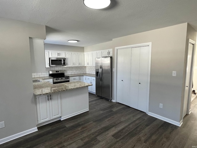 kitchen with light stone counters, kitchen peninsula, stainless steel appliances, decorative backsplash, and white cabinets