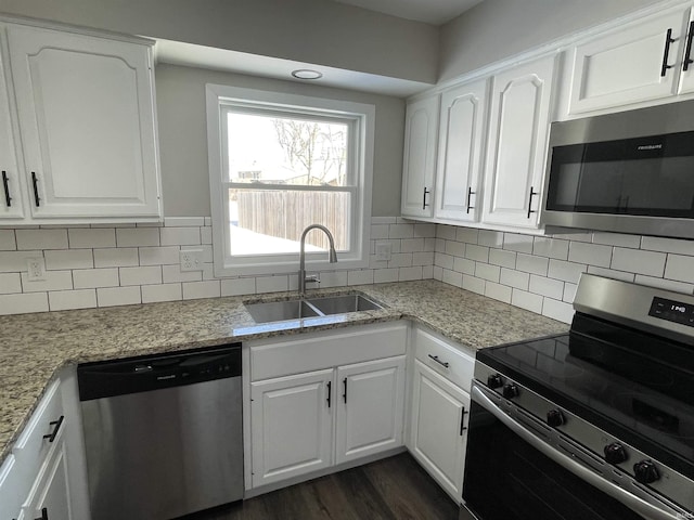 kitchen with stainless steel appliances, white cabinets, sink, and light stone countertops