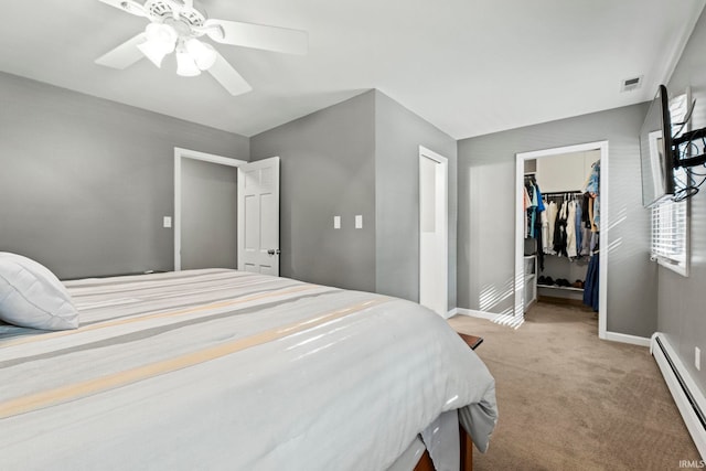 bedroom with a closet, a baseboard heating unit, carpet flooring, a walk in closet, and ceiling fan