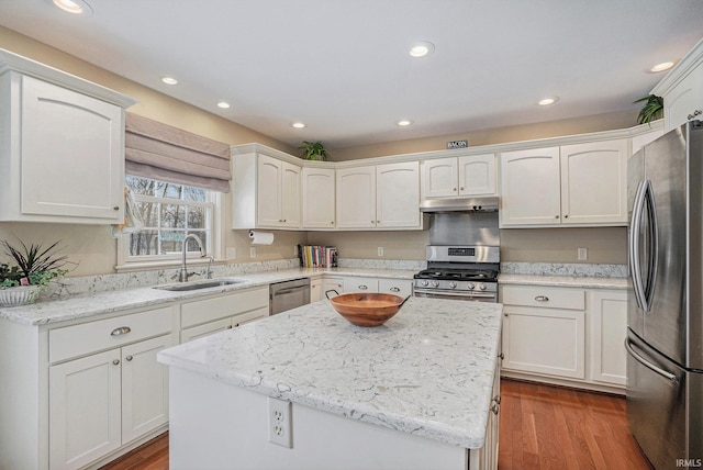 kitchen featuring hardwood / wood-style floors, stainless steel appliances, a center island, light stone countertops, and sink