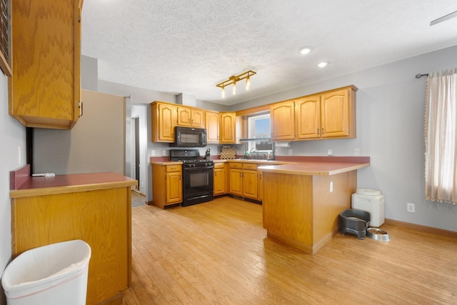 kitchen with black appliances, light hardwood / wood-style floors, kitchen peninsula, a breakfast bar, and sink