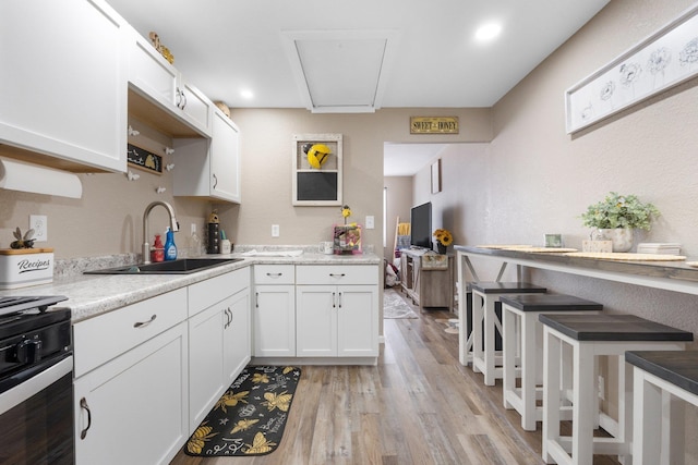 kitchen with sink, white cabinets, stove, and light hardwood / wood-style flooring