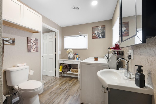 bathroom featuring washer and dryer, toilet, vanity, and hardwood / wood-style flooring