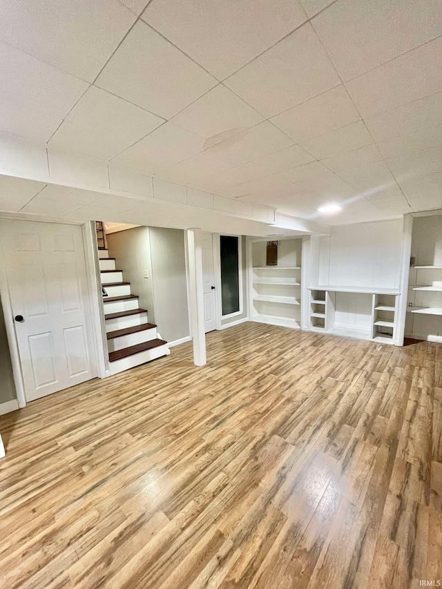 basement with built in shelves and light hardwood / wood-style flooring