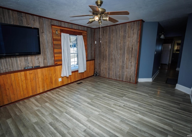 unfurnished living room with ornamental molding, light wood-type flooring, ceiling fan, and wooden walls