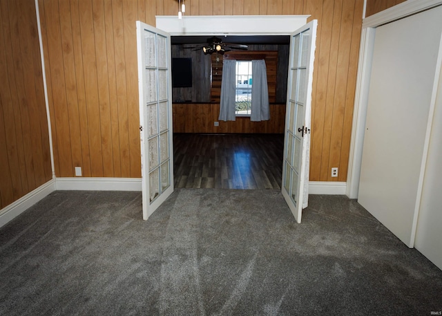 interior space featuring wood walls, ceiling fan, and dark carpet