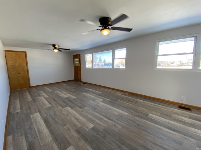 unfurnished room featuring a healthy amount of sunlight, dark wood-type flooring, and ceiling fan