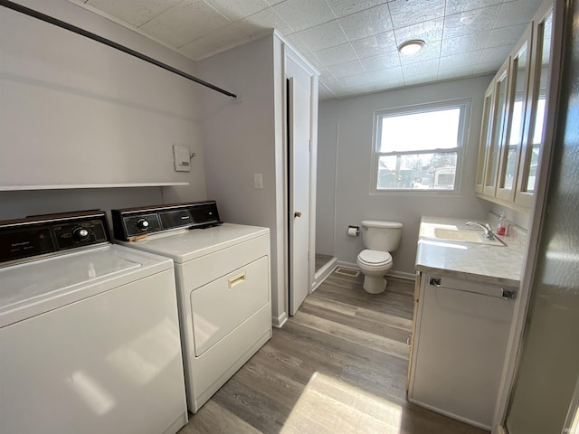 clothes washing area featuring sink, washing machine and clothes dryer, and light wood-type flooring