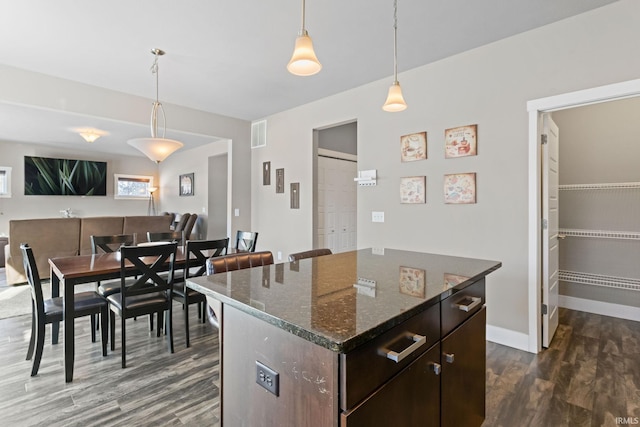 kitchen featuring hanging light fixtures, a center island, dark hardwood / wood-style flooring, dark stone countertops, and dark brown cabinets