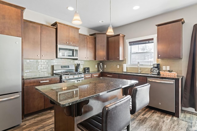 kitchen featuring stainless steel appliances, sink, a kitchen bar, a kitchen island, and dark hardwood / wood-style flooring