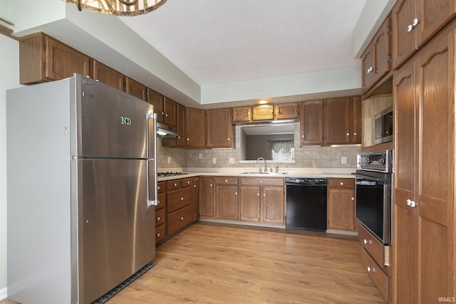 kitchen featuring sink, light hardwood / wood-style floors, backsplash, and black appliances