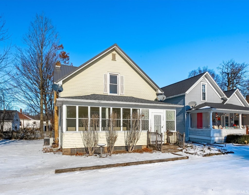 snow covered rear of property featuring central AC unit and a sunroom