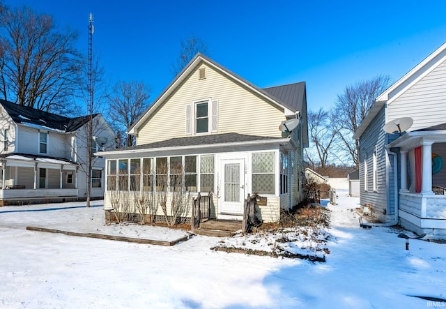 snow covered back of property with a sunroom