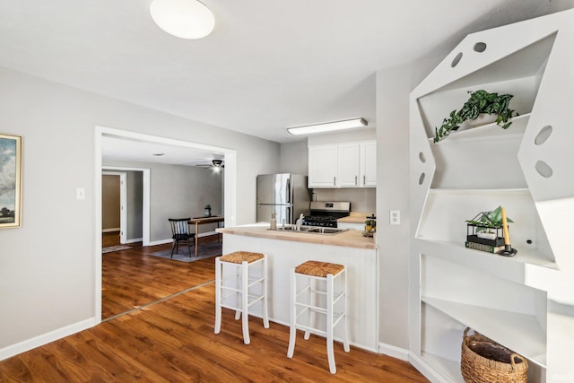 kitchen with stainless steel appliances, white cabinetry, a kitchen breakfast bar, kitchen peninsula, and dark hardwood / wood-style floors