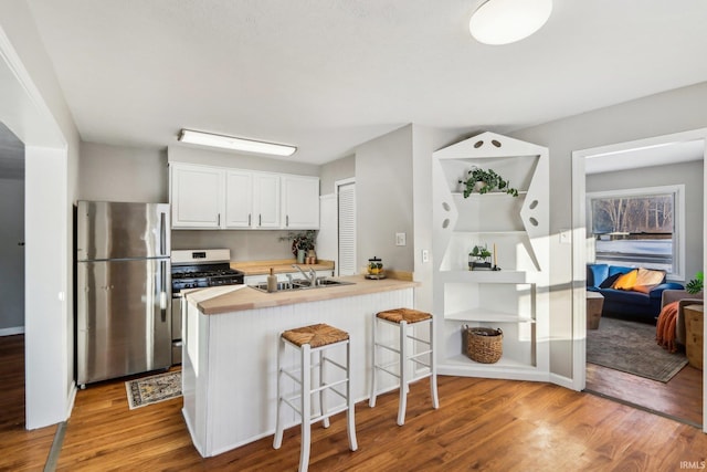 kitchen with kitchen peninsula, a kitchen bar, white cabinetry, appliances with stainless steel finishes, and sink