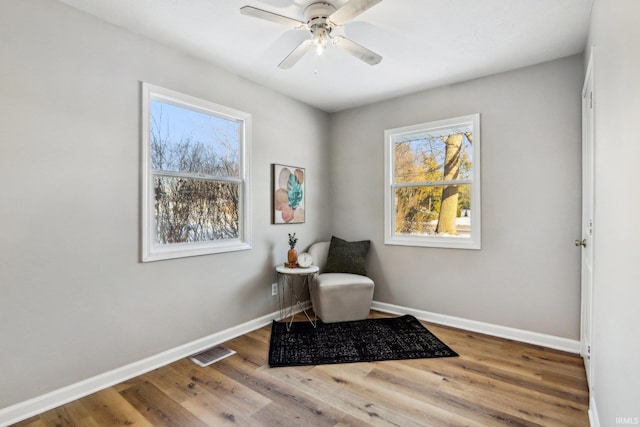 living area with ceiling fan, a wealth of natural light, and wood-type flooring