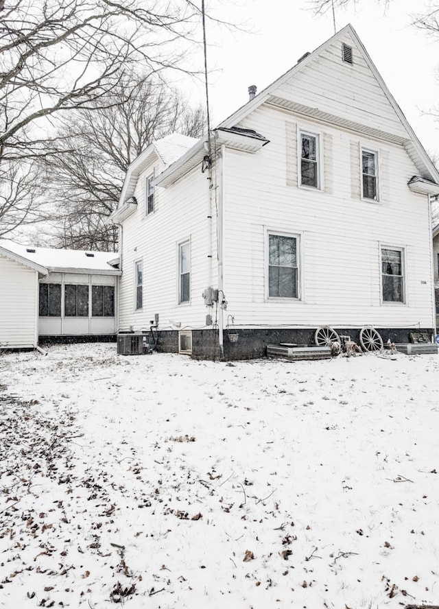 snow covered rear of property featuring a sunroom