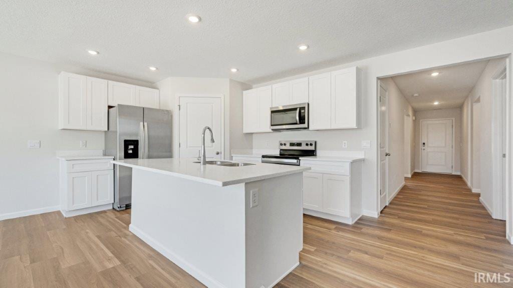 kitchen with stainless steel appliances, white cabinetry, sink, and a kitchen island with sink