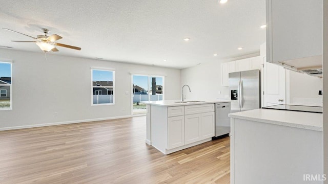 kitchen with appliances with stainless steel finishes, an island with sink, white cabinets, light hardwood / wood-style flooring, and sink